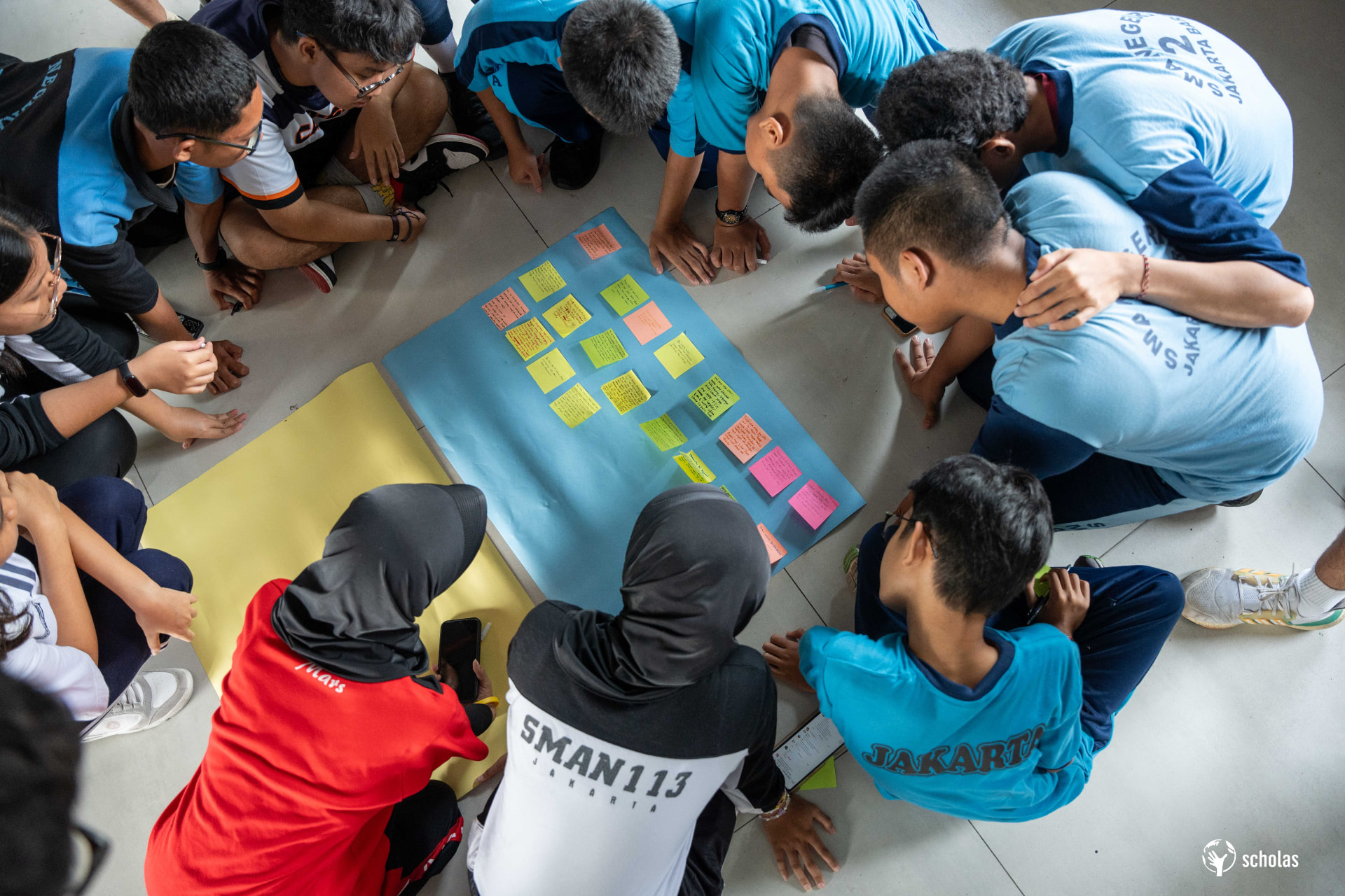 Estudiantes trabajando con papeles y notas en el piso durante un taller de Scholas en Jakarta